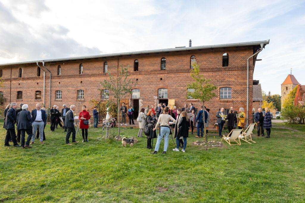 Menschen stehen in kleinen Gruppen im Garten vor einem alten Backsteingebäude