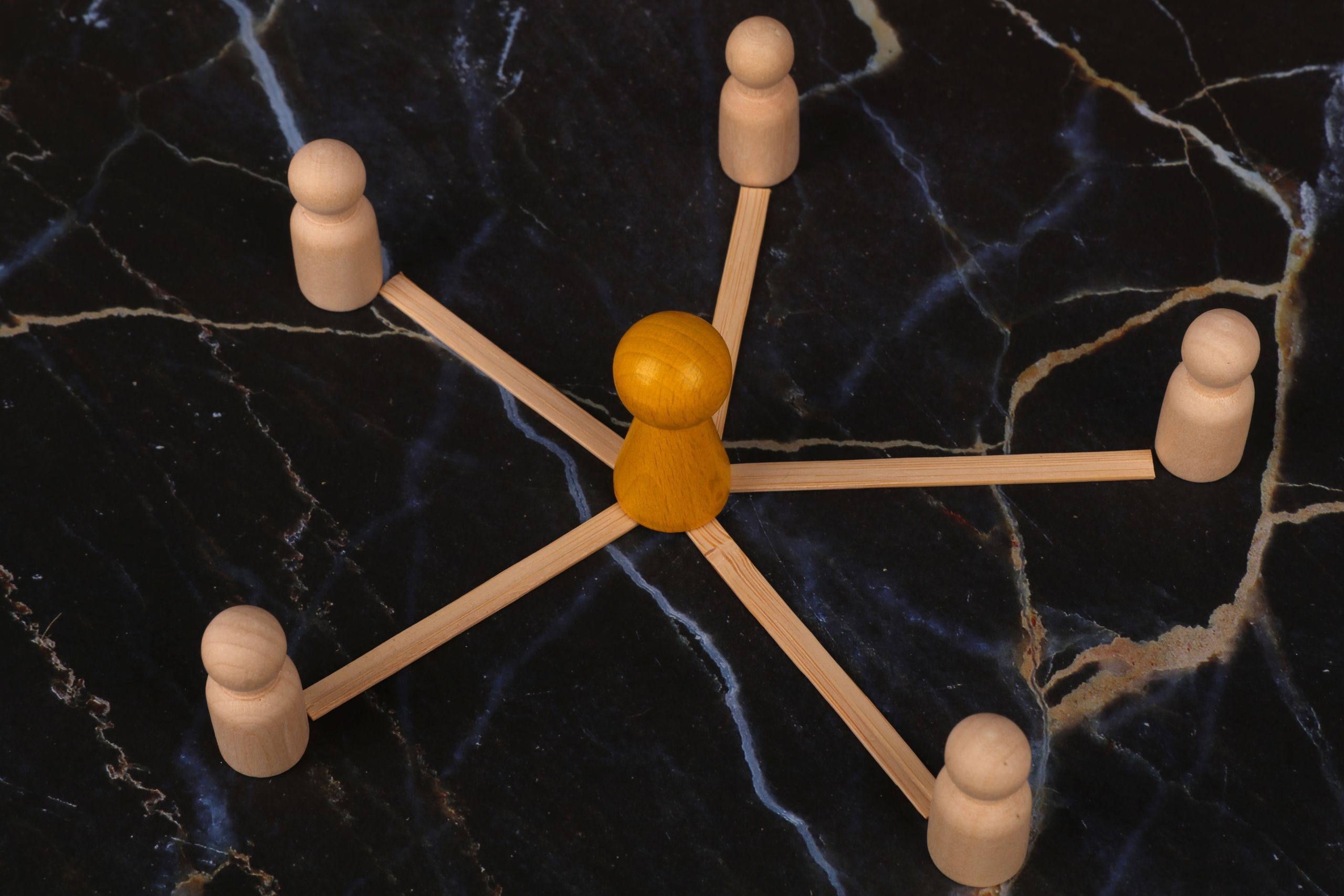 Wooden figures arranged in network pattern on dark marble background, symbolizing communication.