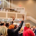 A diverse group of people participating in a worship service, hands raised in devotion.