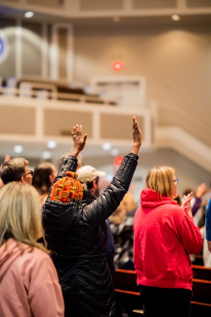 A diverse group of people participating in a worship service, hands raised in devotion.